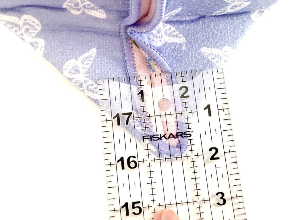 A clear ruler marked "Fiskars" measures the length of a blue fabric with white butterfly prints and a pink zipper.