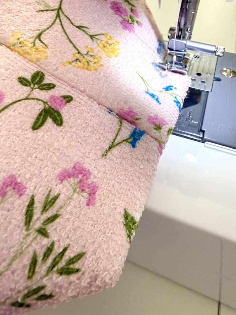Close-up of a sewing machine stitching pink fabric with embroidered flowers in yellow, blue, and pink.