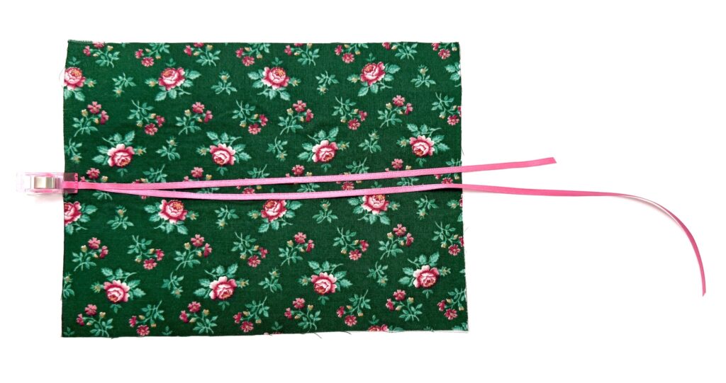 A rectangular tea wallet made of green floral fabric with two pink plastic ties and a pink clip attached to one side.