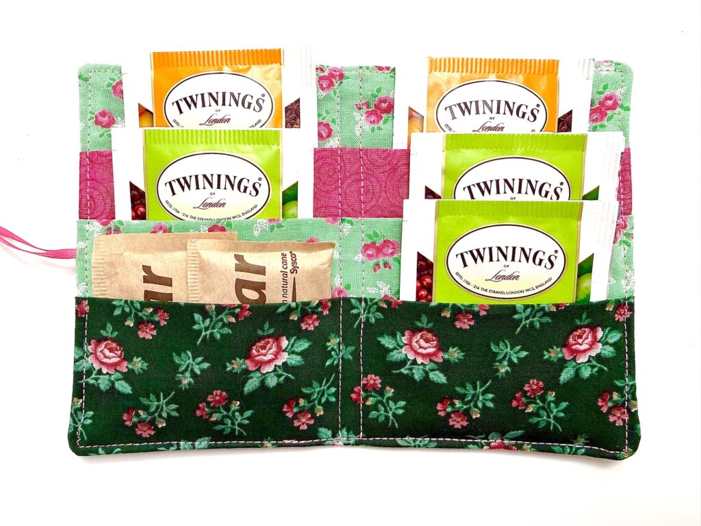 A floral fabric tea wallet holds assorted Twinings tea sachets and packets of sugar, neatly organized in pockets.