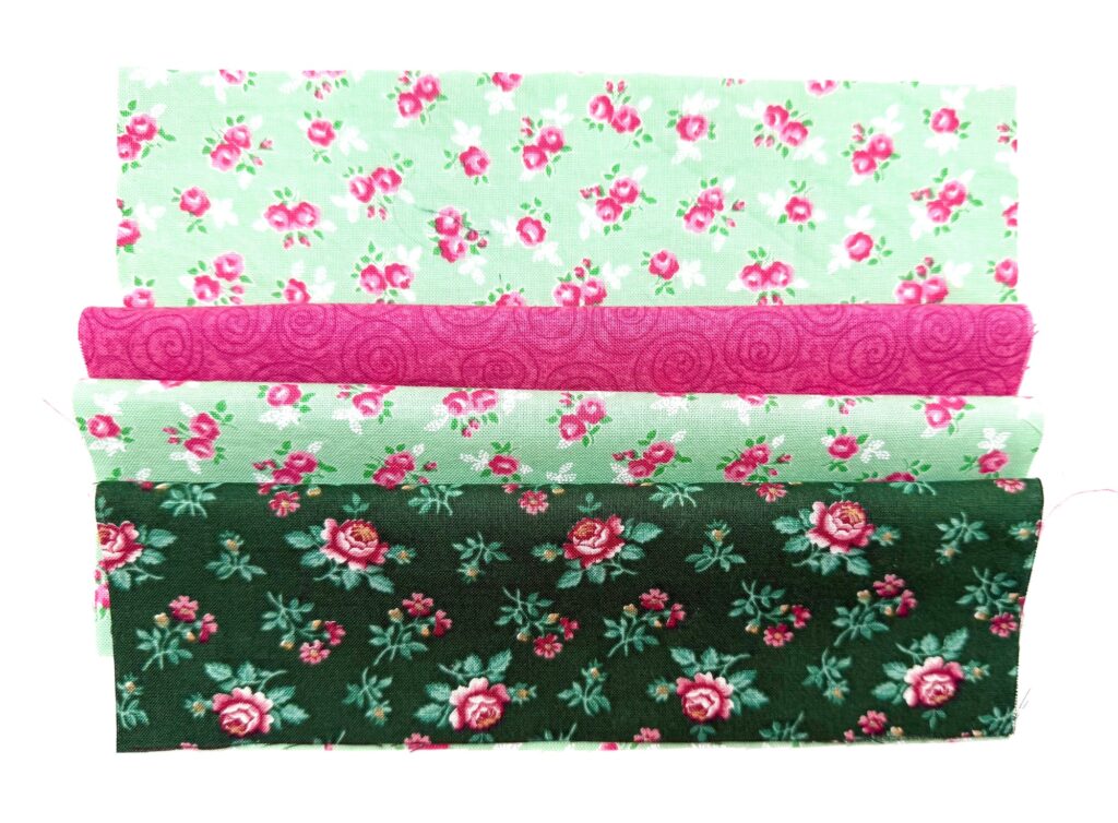 Three fabric strips with floral patterns, perfect for a tea wallet: light green with small pink flowers, bright pink with swirls, and dark green with larger pink roses.