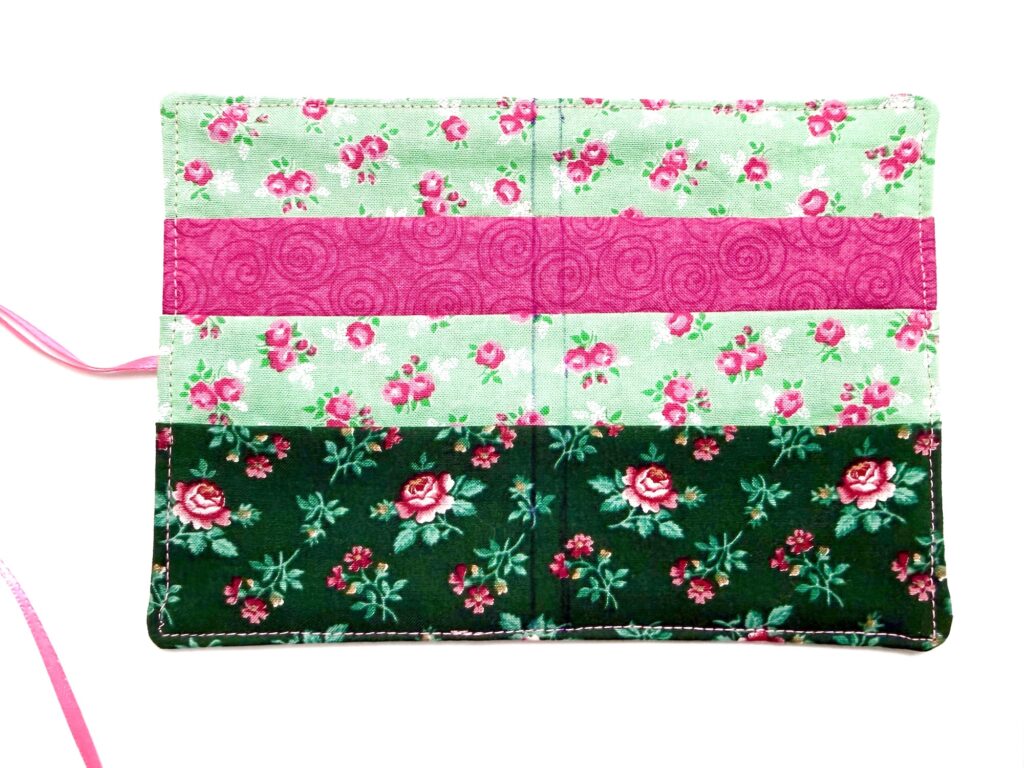 A tea wallet fabric cover with floral patterns in green and pink tones, featuring two pockets and a pink ribbon attached on the left side.