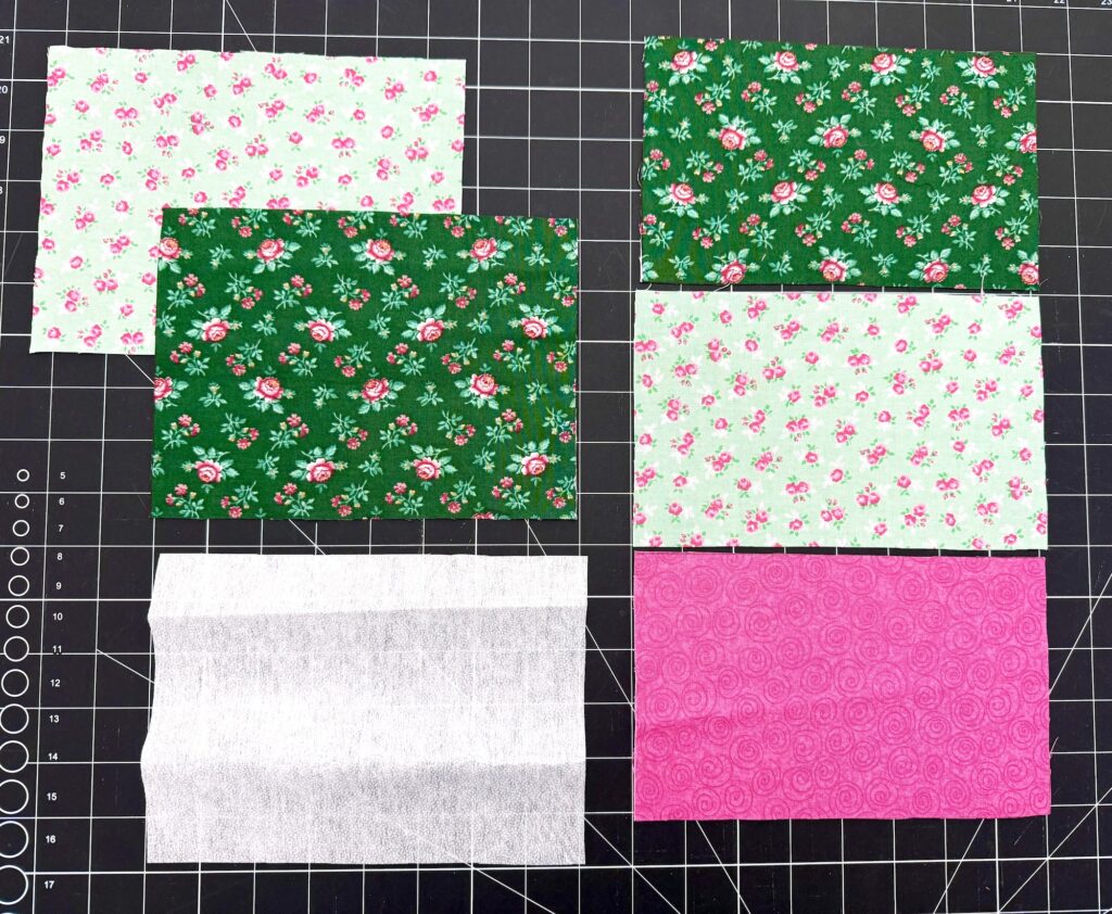 Six rectangular fabric pieces with various floral patterns and solid colors are arranged on a cutting mat with gridlines, ready to be crafted into a charming tea wallet.