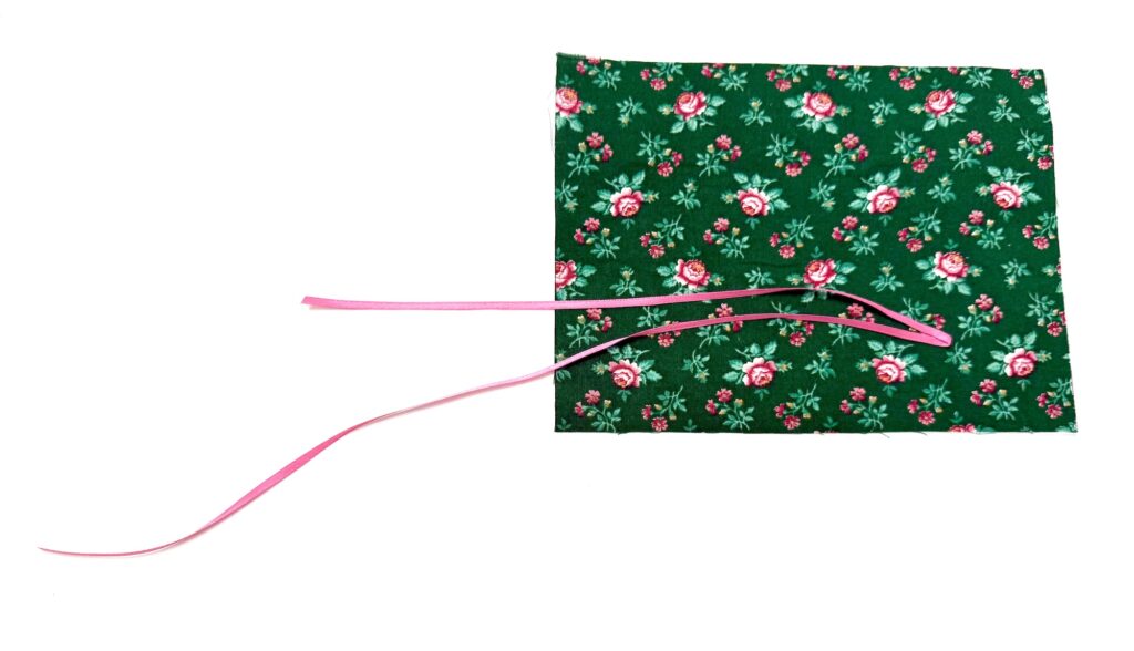 A piece of green floral fabric, perfect for a tea wallet, with pink ribbon threaded through a seam on a white background.