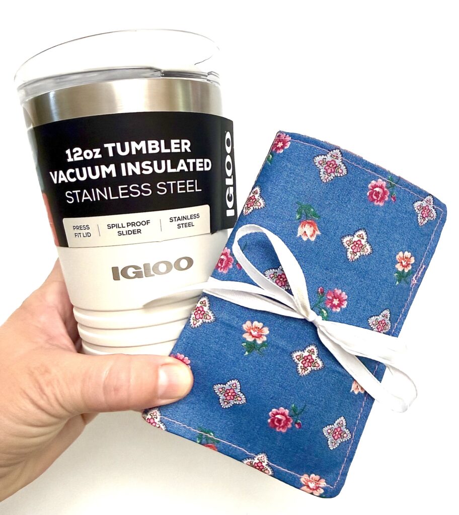 A hand holds a stainless steel 12oz Igloo insulated tumbler and a blue floral-patterned tea wallet pouch tied with a white ribbon.