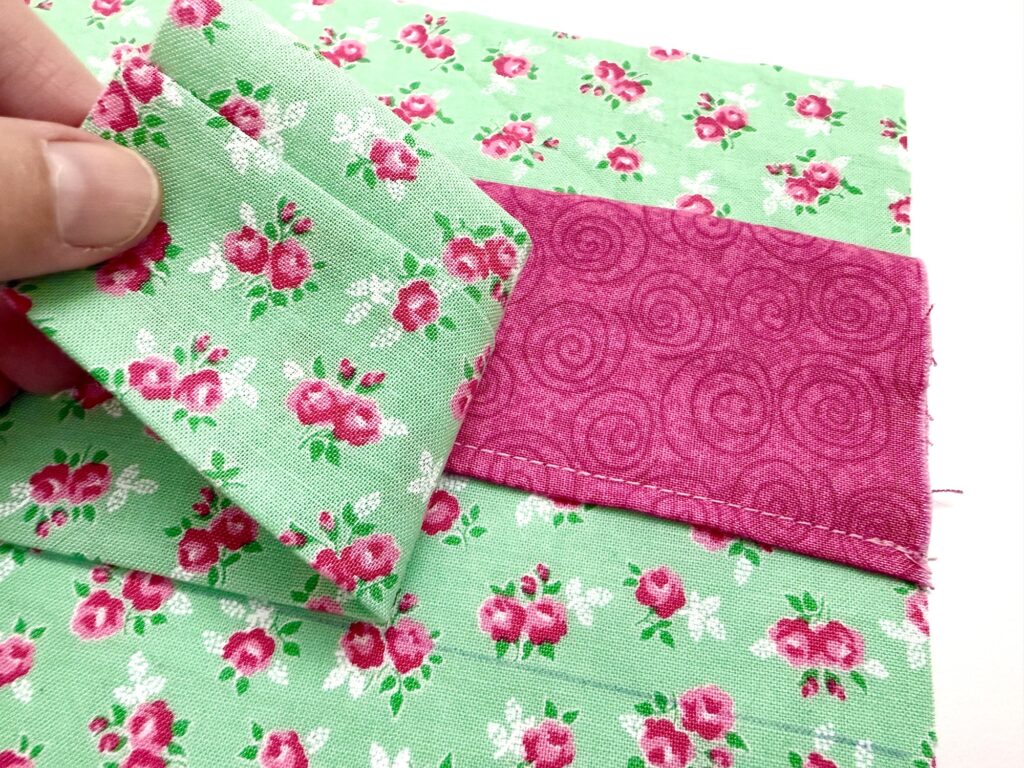A hand holds a piece of green floral fabric next to a pink strip sewn onto green floral fabric, showing part of a tea wallet sewing project.