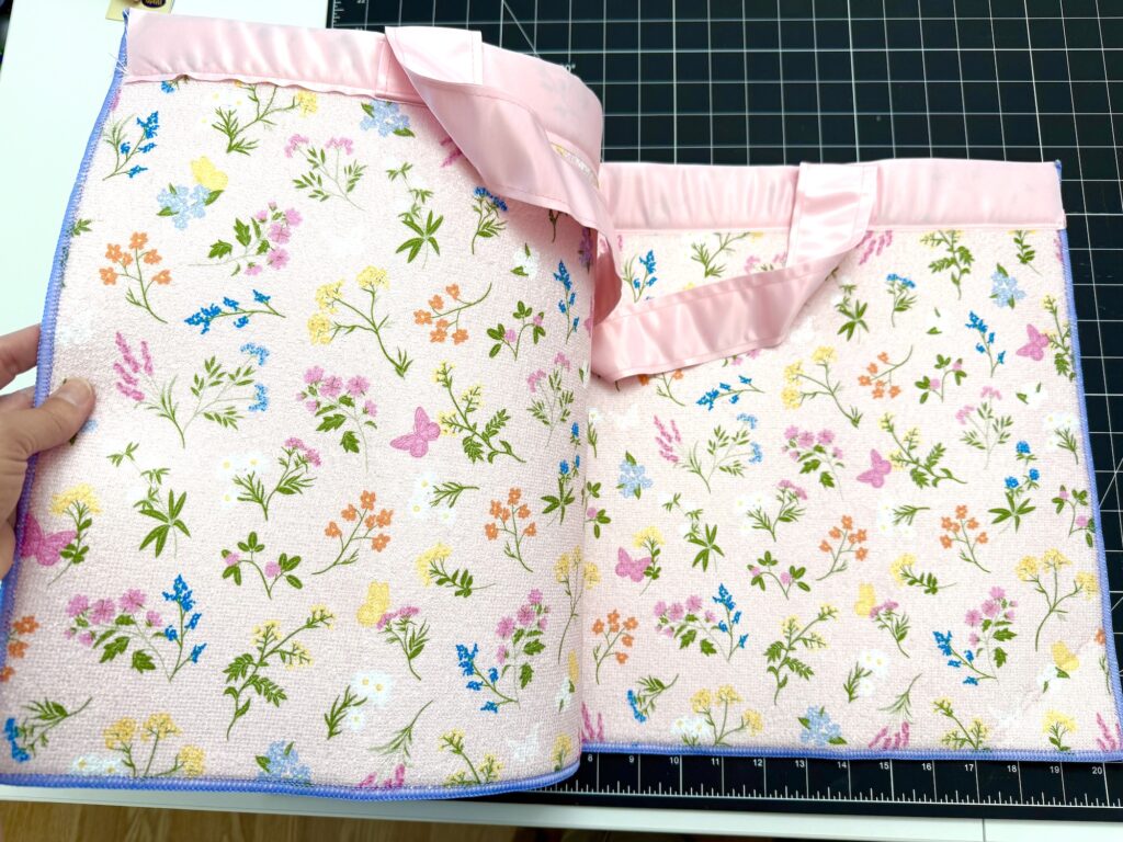 Two pastel pink tote bags with floral patterns and satin handles are displayed on a black cutting mat.
