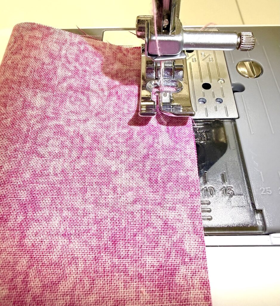 A close-up view of a sewing machine stitching a piece of pink fabric, perfect for crafting a charming tea wallet.