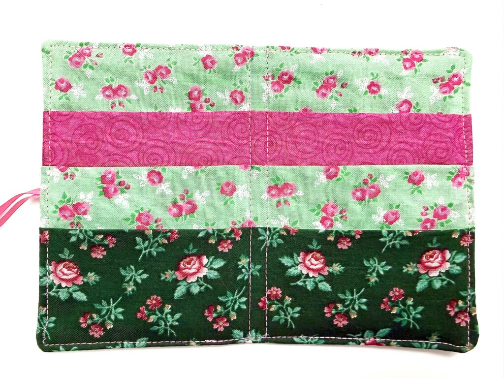 Rectangular fabric tea wallet with three horizontal sections of floral patterns in pink, light green, and dark green, stitched together with visible seams.