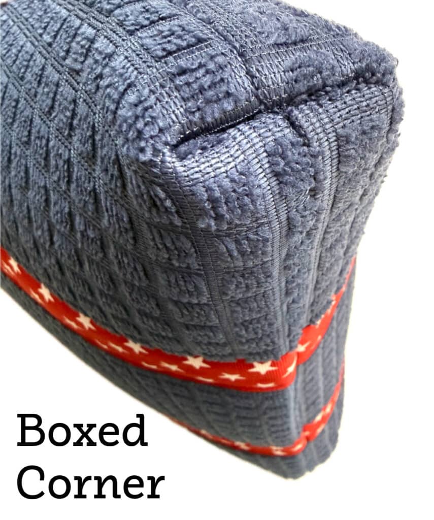 Close-up of a blue textured fabric cushion with a boxed corner and a red ribbon with white stars wrapped around it. Text reads “Boxed Corner.”.