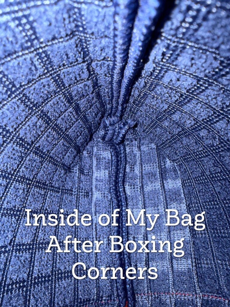 Close-up view of the inside of a fabric bag with boxed corners, showing blue and gray plaid material and visible stitching. Text overlay reads, “Inside of My Bag After Boxing Corners.”.