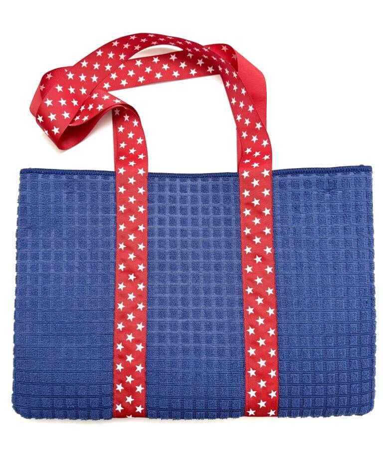 A blue textured tote bag with red straps decorated with white stars, displayed on a white background.