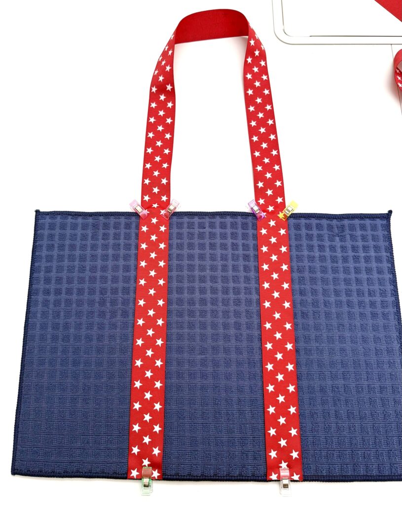 A blue textured fabric dish mat bag with two red straps featuring white stars clipped vertically along its length, set on a white surface.
