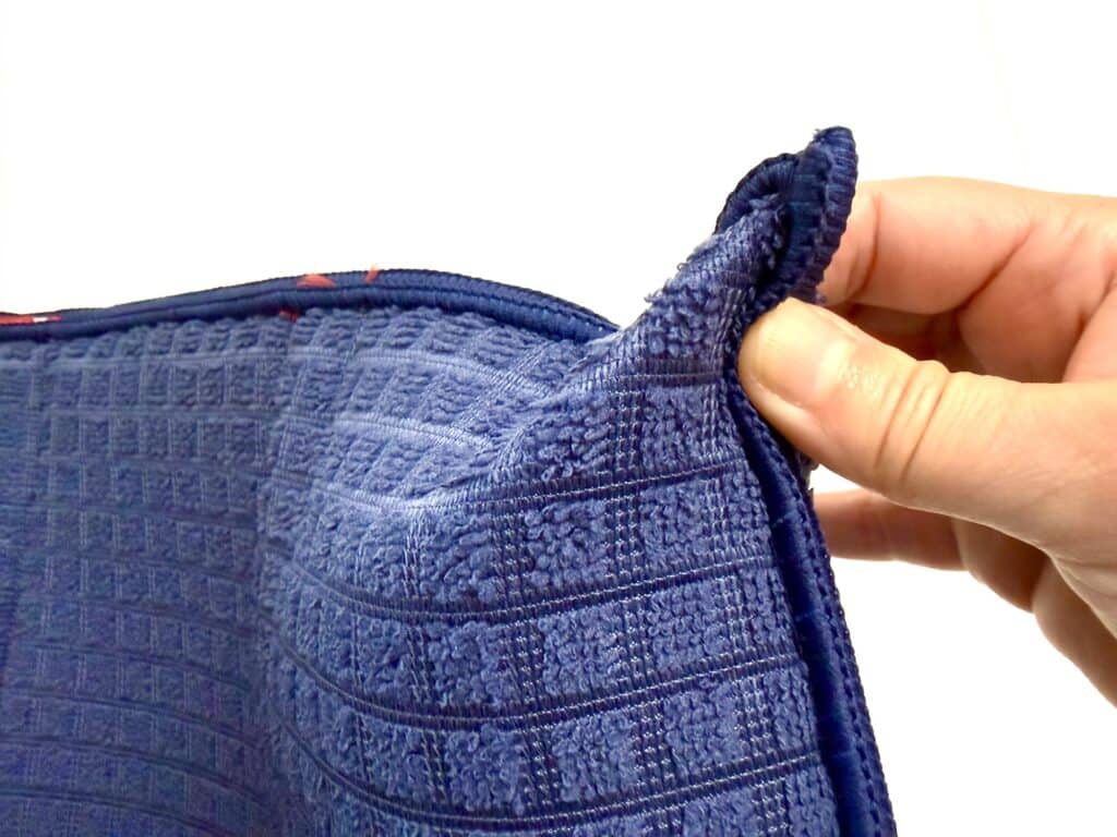 A hand holding the corner of a blue textured towel against a white background.