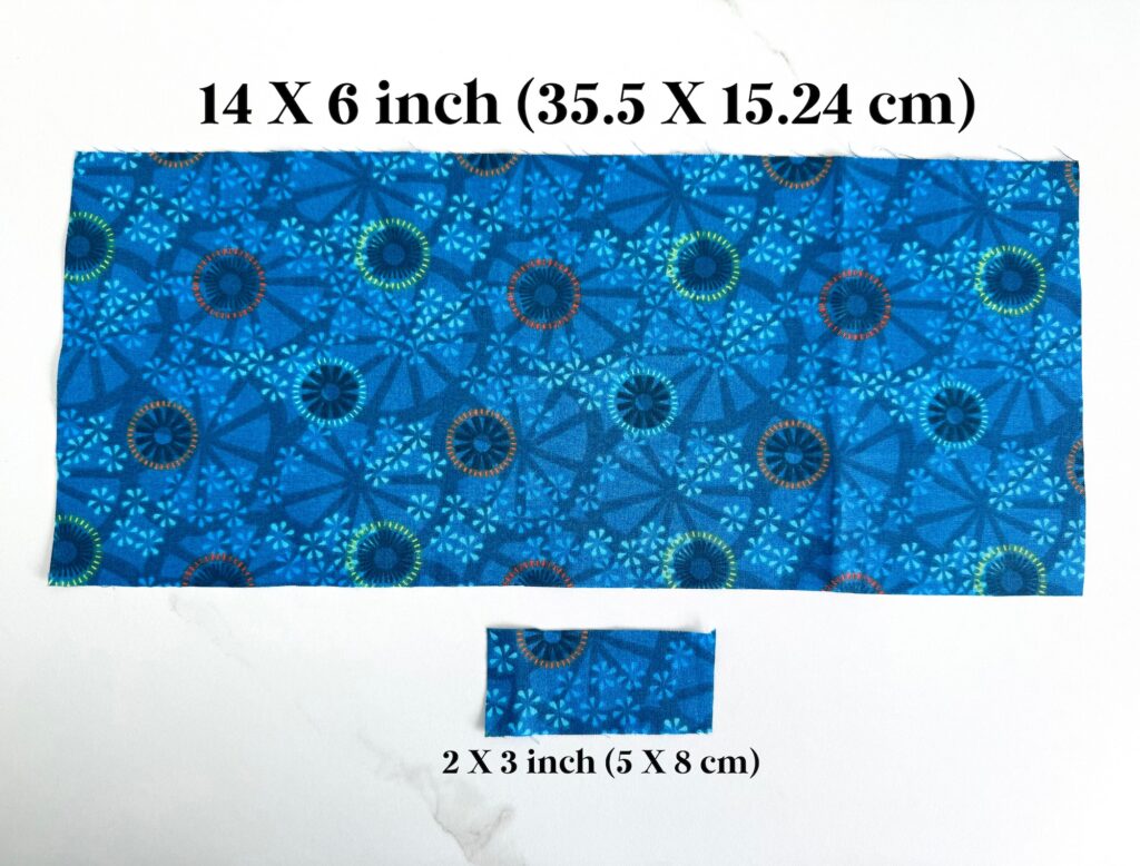 Two blue fabric pieces with geometric patterns, one measuring 14 x 6 inches (35.5 x 15.24 cm) and another 2 x 3 inches (5 x 8 cm), displayed on a white surface.