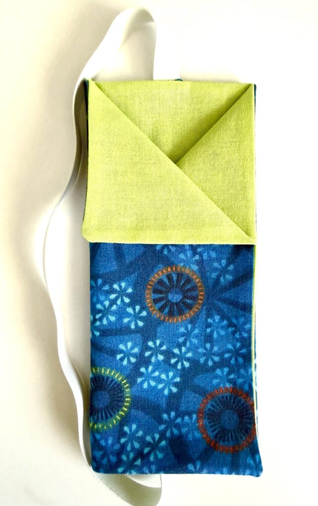 A small fabric bag with a blue patterned body, a green triangular flap, and a white strap, photographed on a white background.
