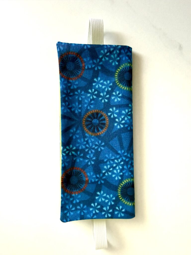 A rectangular blue fabric pouch with circular patterns and a white elastic loop at the top, placed on a white surface.