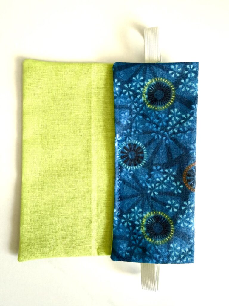 Two rectangular fabric pouches, one solid light green and one blue with a circular pattern and a white elastic loop, are placed side by side on a white surface.