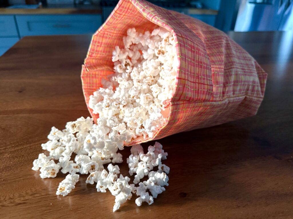 A bag of popcorn tipped over on a wooden table, with popcorn spilling out onto the surface.