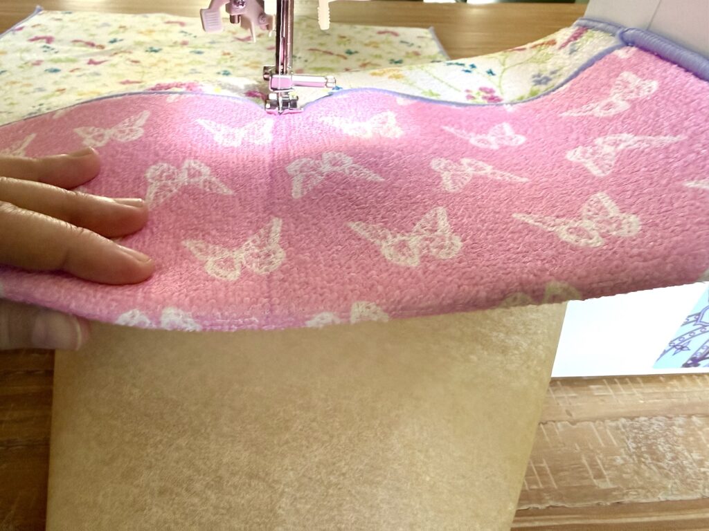 A person uses a sewing machine to stitch pink butterfly-patterned fabric layered over beige material.