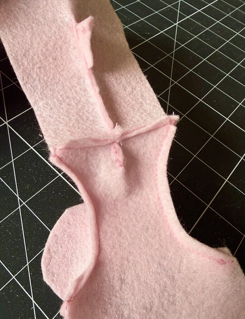 Piece of pink felt fabric with seams sewn, placed on a black cutting mat with a white grid pattern.