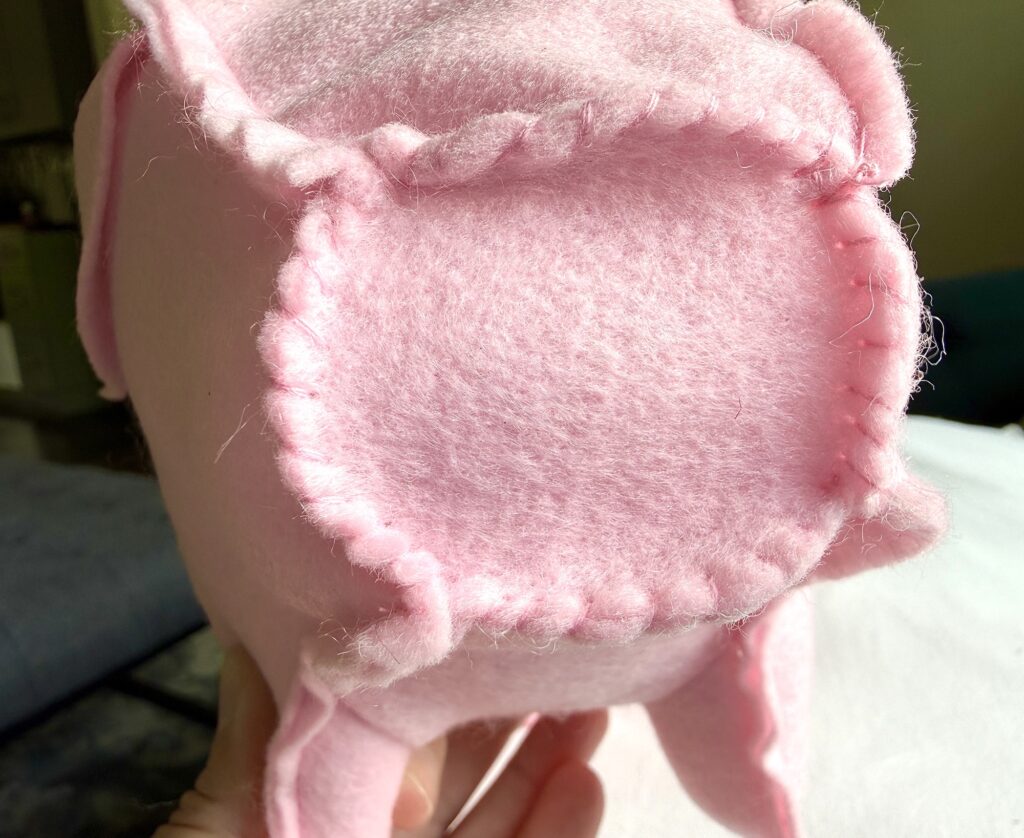 Close-up of a hand holding a pink, hand-stitched felt object with visible seams, possibly a soft toy or pillow.