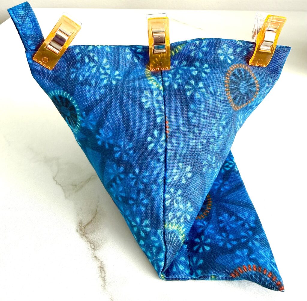 A blue fabric piece with circular patterns is folded and held together at the top by three orange clips, resting on a white surface.