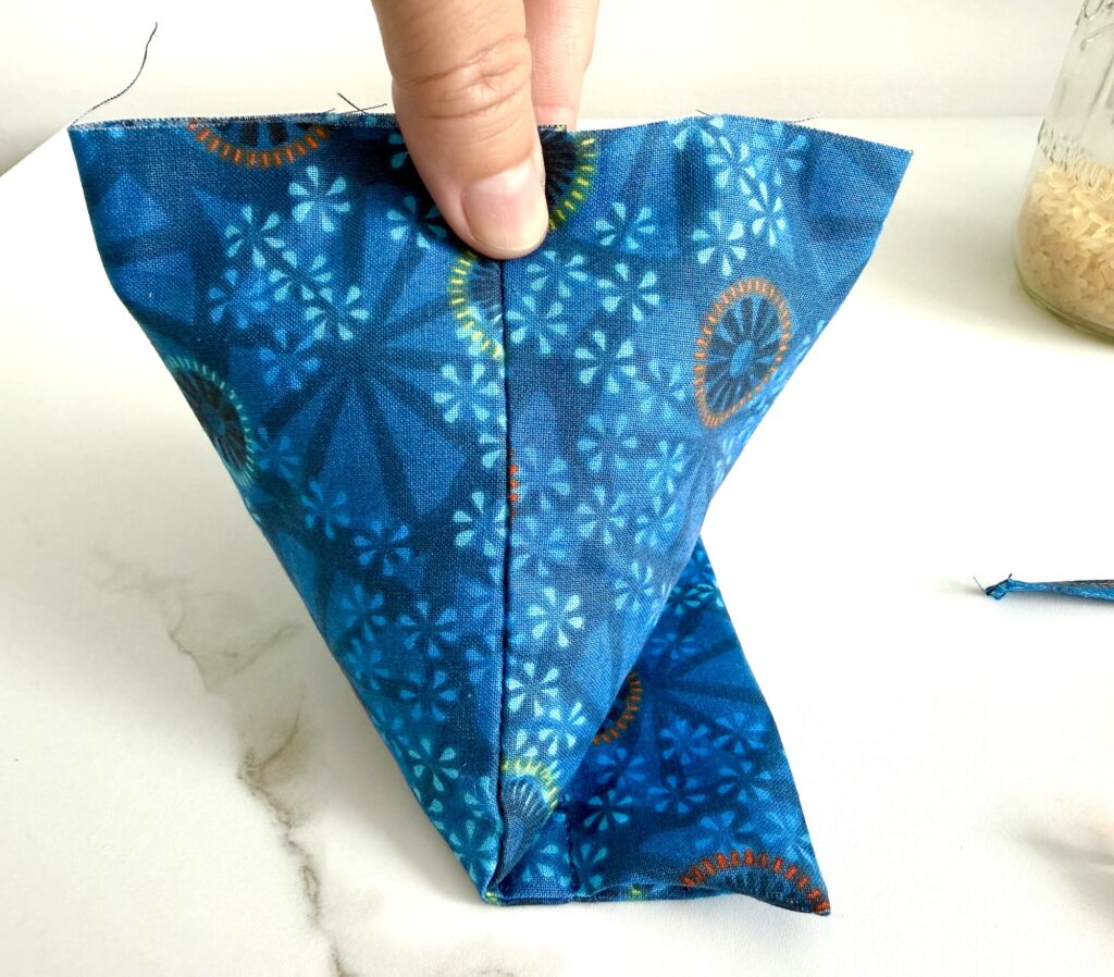 A hand holds a piece of blue patterned fabric sewn into a cone shape on a white surface.