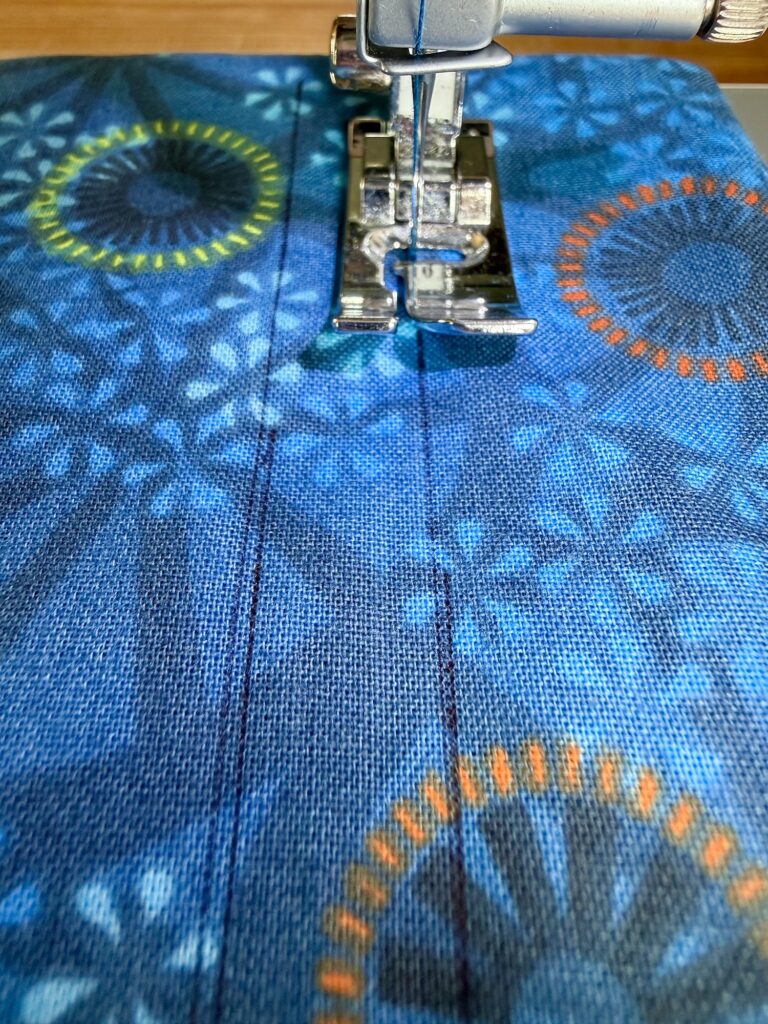 Close-up of a sewing machine needle stitching straight lines on blue patterned fabric with circular designs.