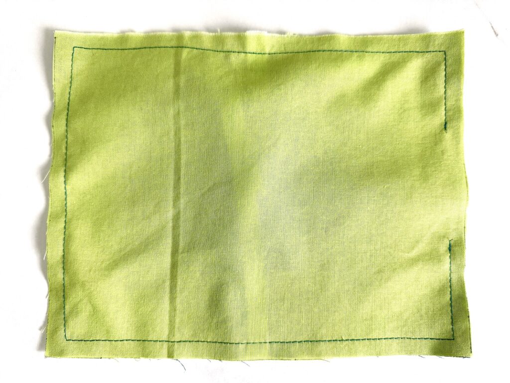 A rectangular piece of green fabric with a stitched border in dark thread, placed on a white surface.