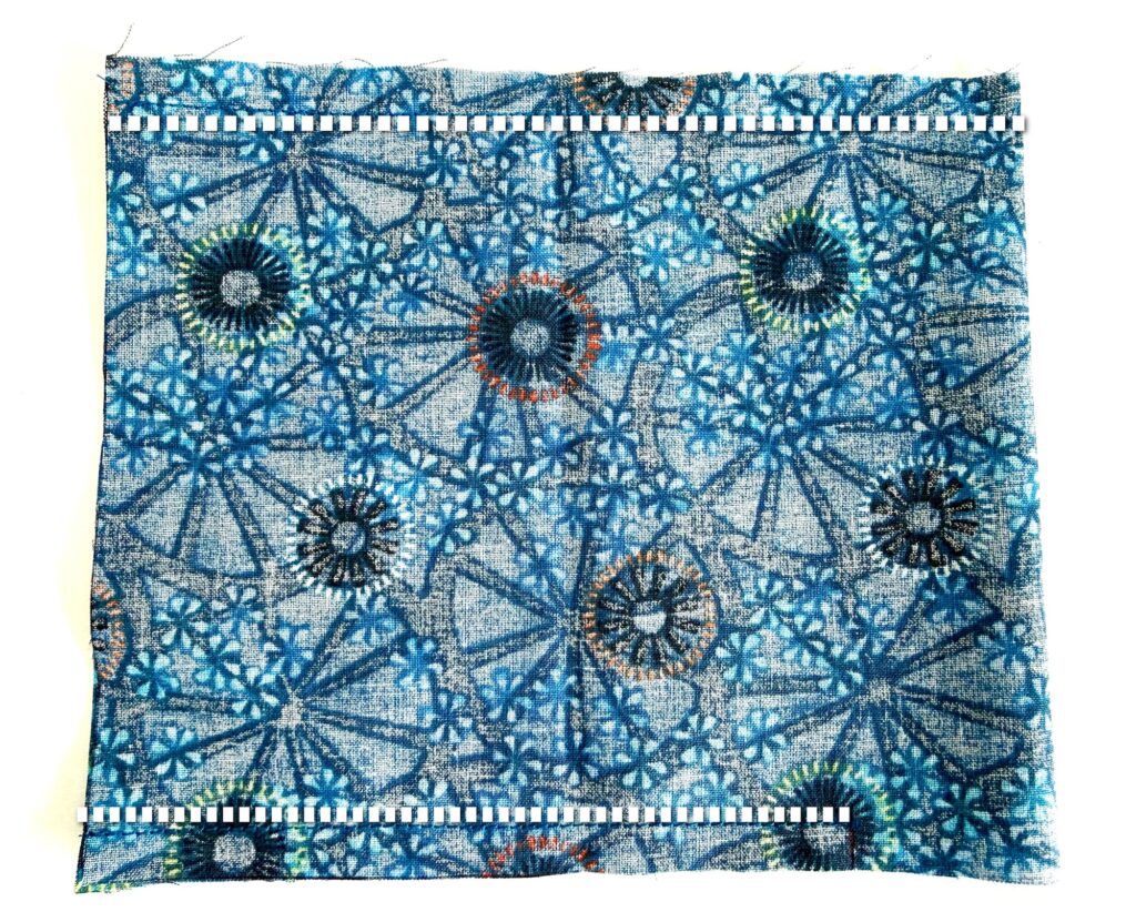 A rectangular piece of blue fabric with circular and floral patterns, bordered by black and white stitched lines along the top and bottom edges.