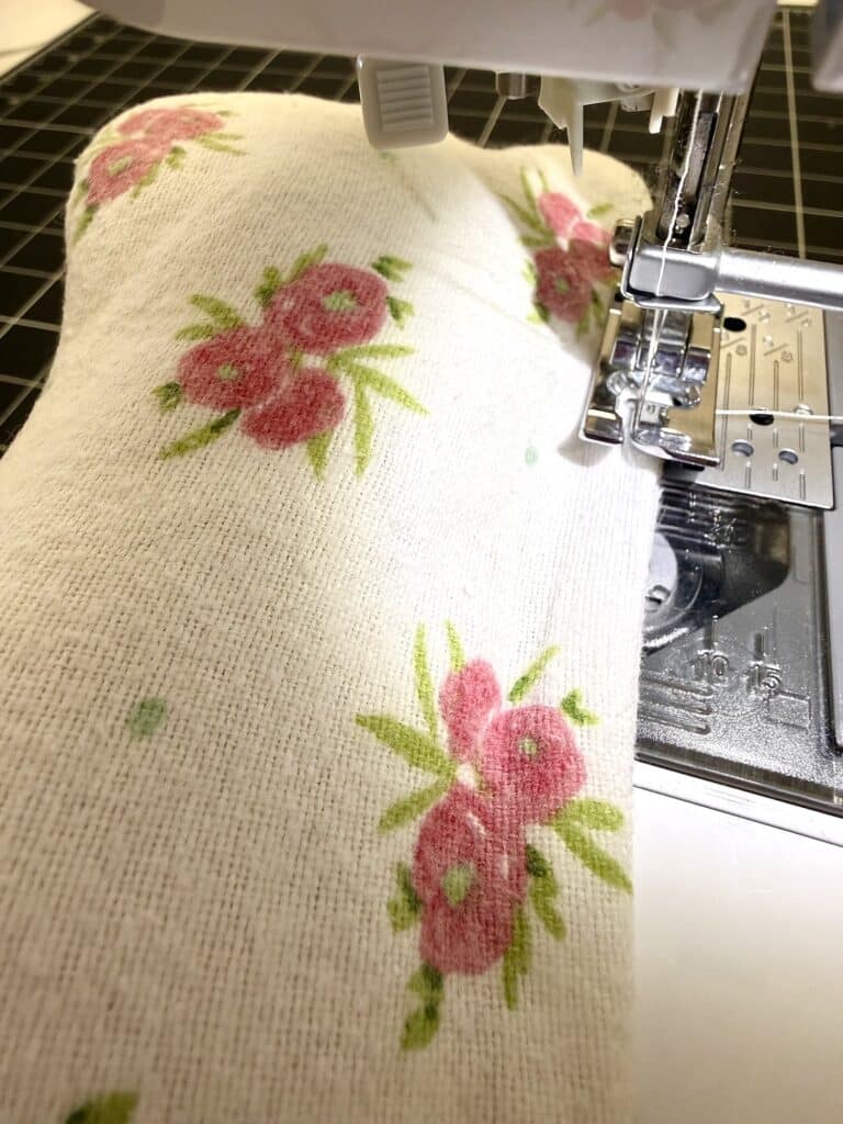 A close-up view of a sewing machine stitching a piece of white fabric with pink floral patterns.