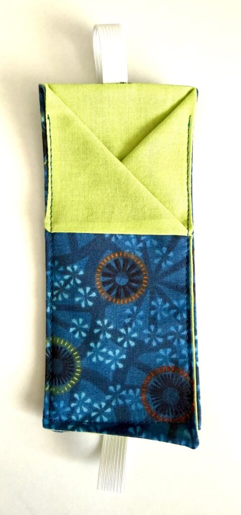 A fabric pouch with a green top, blue patterned bottom, and white loop attached, displayed on a white background.