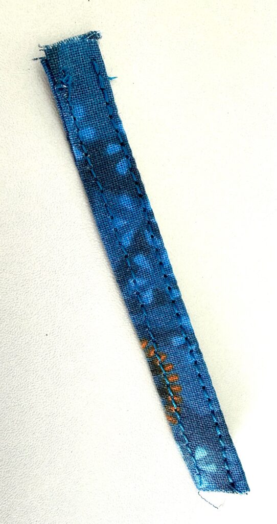 A narrow strip of blue fabric with visible stitches lies on a white surface.