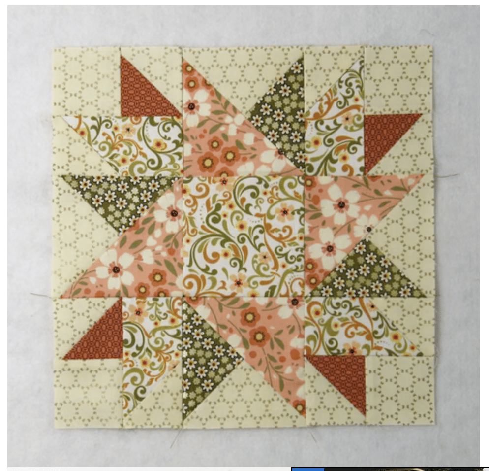 Patchwork quilt block with a star pattern, featuring floral and geometric fabrics in shades of cream, green, orange, and pink.