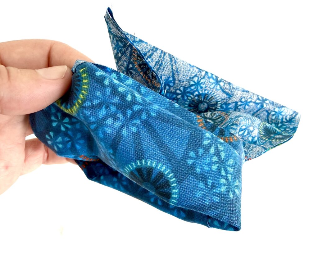 A hand holds a piece of folded blue fabric with circular and floral patterns, against a white background.