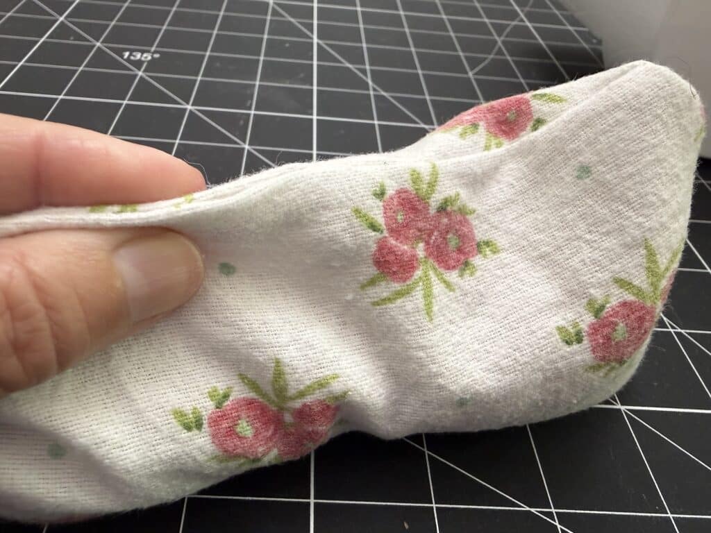 A hand holds a piece of white fabric with a pink floral pattern over a black grid cutting mat.