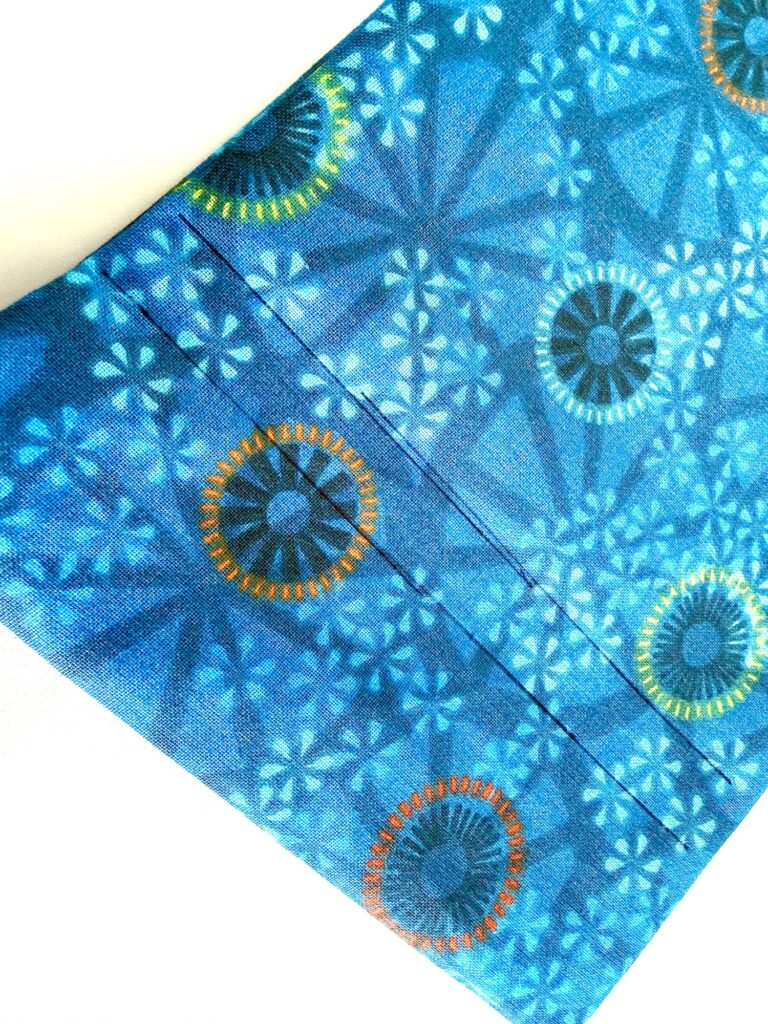A piece of blue fabric with geometric and circular patterns in orange, yellow, green, and white, shown at a diagonal angle.