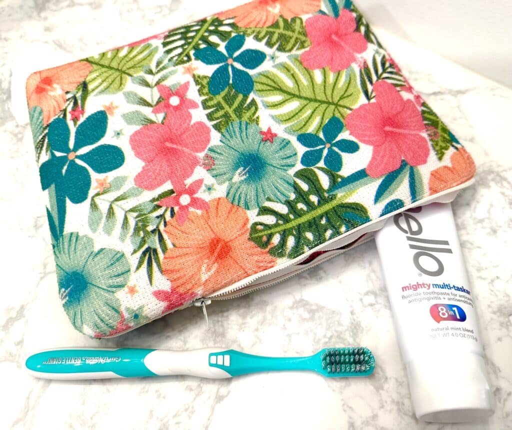 A floral pouch, a tube of Hello toothpaste, and a turquoise toothbrush are arranged on a marble surface.