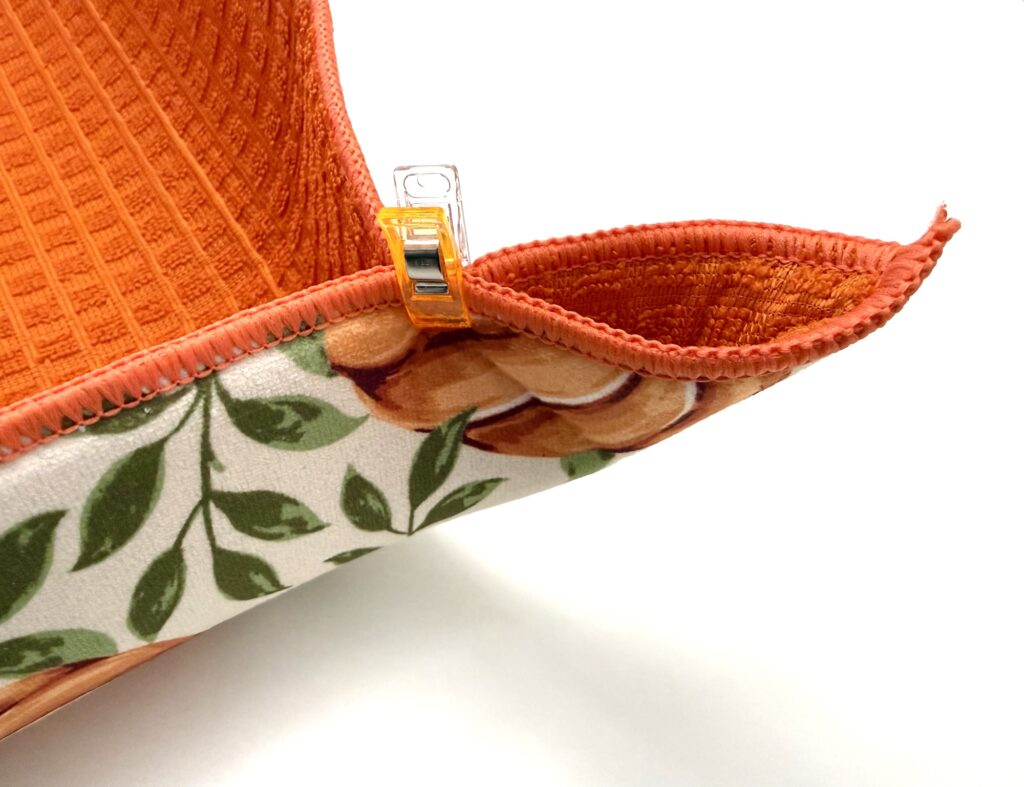 sewing clip holds together the pinched corners of an orange colored drying mat decorated with pumpkins