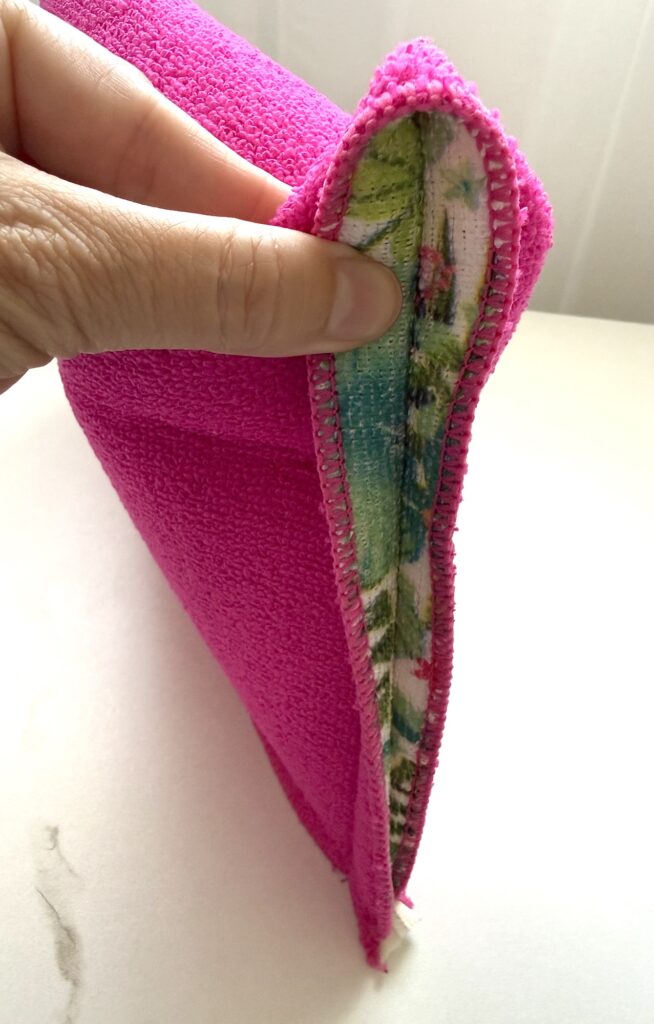 A hand holds open the corner of a bright pink fabric pouch, revealing a floral-patterned lining and visible stitching along the edge.