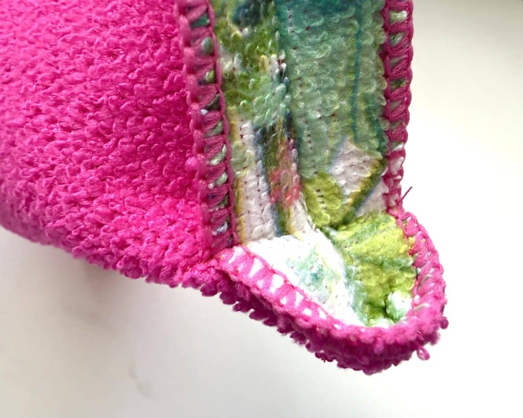 Close-up of the corner of a pink terry cloth item with multicolored inner fabric and visible stitching.