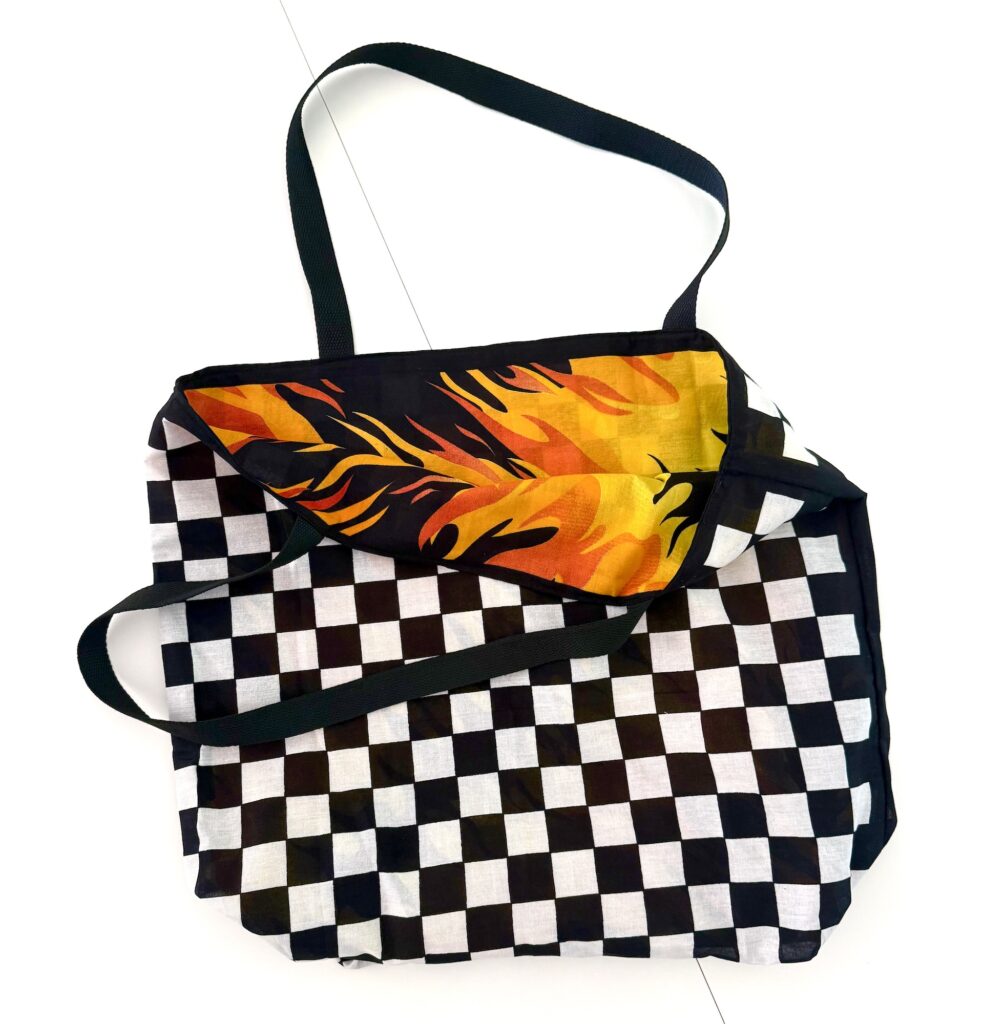 A bandana bag with a black-and-white checkerboard pattern and a flap featuring orange and yellow flame graphics, shown on a white background.