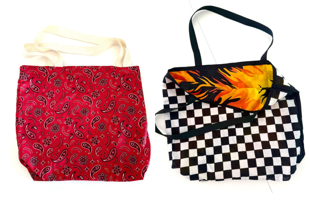 Two fabric tote bags: one is a bandana bag in red with a white paisley pattern and cream handles, while the other features a black-and-white checkerboard pattern with a flame-patterned flap.