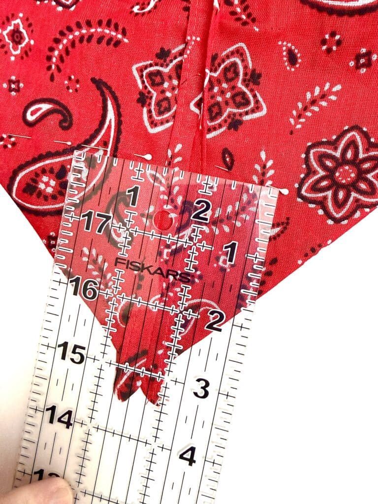A clear ruler measures the width of a red paisley-patterned fabric folded to a point, showing a width of approximately 2.5 inches.