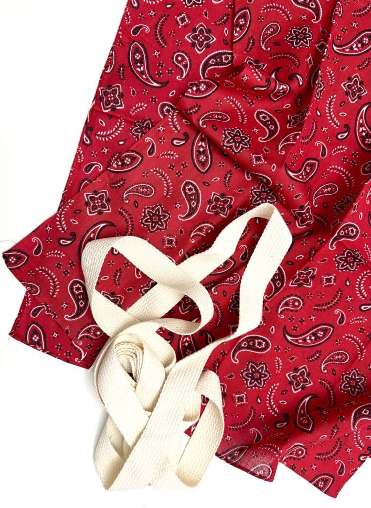 Red paisley-patterned fabric with two off-white, flat woven straps lying on it, arranged on a white background.