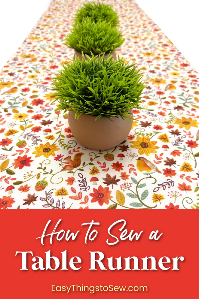 Three small potted artificial grasses sit on a table runner patterned with autumn leaves, flowers, squirrels, and birds. Text at the bottom reads, “How to Sew a Table Runner, EasyThingstoSew.com.”
