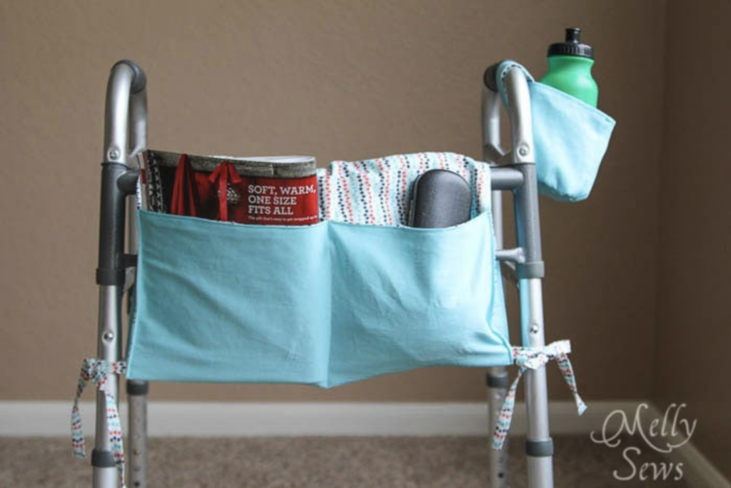 Light blue fabric walker caddy with two front pockets holding a magazine and glasses case, and a side pocket holding a green water bottle.