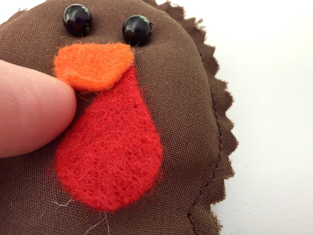 A finger touches the felt red wattle of a brown fabric turkey craft.