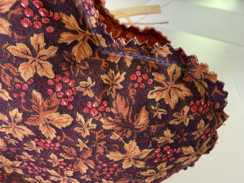 A heart-shaped fabric ornament with a dark purple autumn-themed print of gold leaves and red berries, featuring a raw, pinked edge.